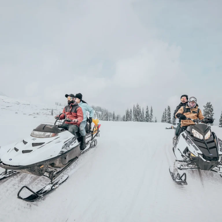 Two travellers on snowmobiles riding across a snowfield in Kashmir