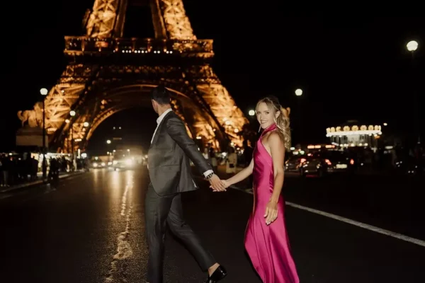 Couple walking in front of the illuminated Eiffel Tower at night