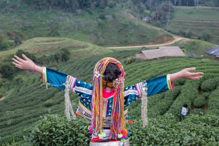 Woman in colourful traditional dress with arms outstretched above Assam tea gardens